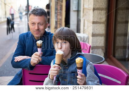 Father and son eating ice-cream in street cafe, family lifestyle. Dad with ofspring enjoying icecream spring outdoor