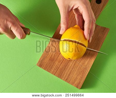 Top view of female hands cut a yellow ripe lemon for preparing a natural diet drink on wooden board on a green background. Health food concept.