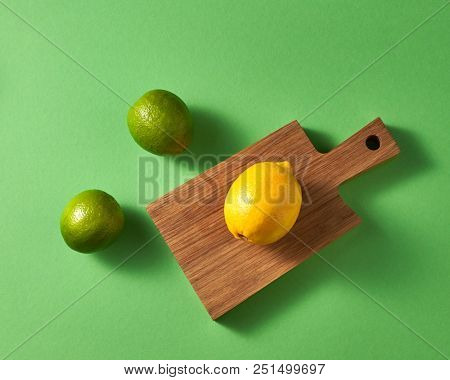Natural organic citrus fruits on a green background. Top view of a group of green limes and one yellow lemon on a wooden cutting board.