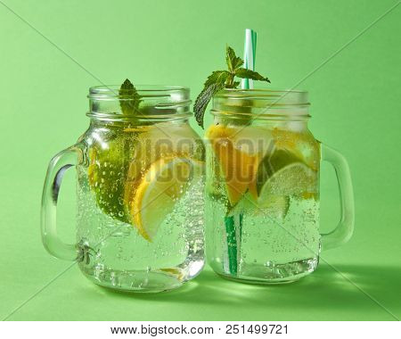 The slices of lemon and lime, cubes of ice, leaf of mint, alcohol and plastic straw in the jars. Concept of cold alcoholic or non-alcoholic summer drinks.