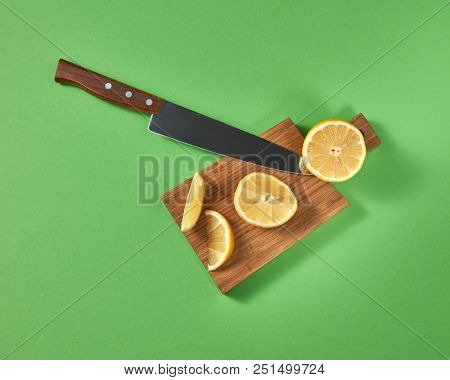 Top view of halfs and slices of natural lemon on a cutting wooden board. A sharp steel knife is cut by organic citrus fruit.