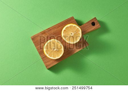 Citrus fruits on a green background with copy space. Top view slices of yellow natural lemon on a wooden board - ingredient for cooking summer homemade drinks.