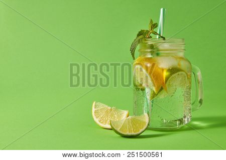 Glass jar on a green table with homemade sparkling non-alcoholic beverage with plastic straw on a green background. Concept of cold alcoholic or non-alcoholic summer drinks.