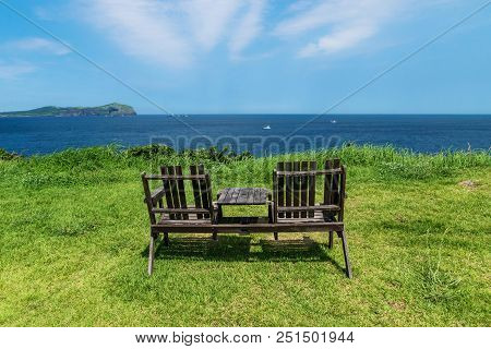 Wooden Chairs On Grass Meadow With View On Ocean And Blue Sky And Udo Island, Jeju Island, South Kor