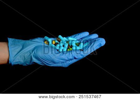 A Hand In A Blue Medical Glove Holds Medications And Pills Of Different Colors On A Black Background