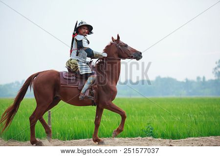 Asian Thai Warrior In Traditional Armor Suit Riding Horse In Rural Farm Background. Vintage Retro Wa