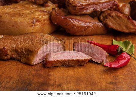 Smoked Meat Sliced On A Wooden Board With Red Pepper And Wooden Background