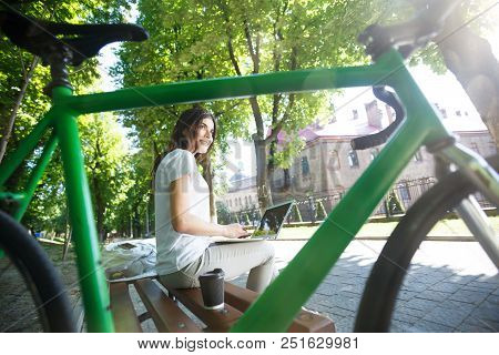 Pretty Girl With Green Bicycle Sitting On Beanch And Working With Laptop In The Sunny Summer Park, S