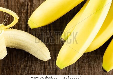 Lot Of Whole Fresh Yellow Banana And One Opened Flatlay On Brown Wood