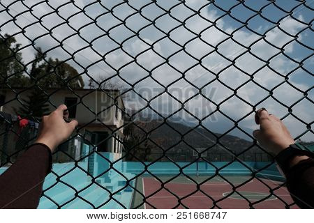 Hands On A Grid In The Background Of A Basketball Court With A View Of The Mountains