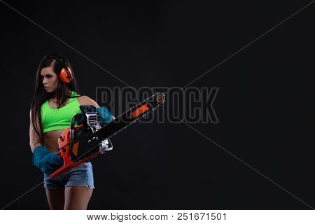 Studio Photography Of A Girl With A Chain Saw On Dark Background. Sexy Builder Woman. Copy Space