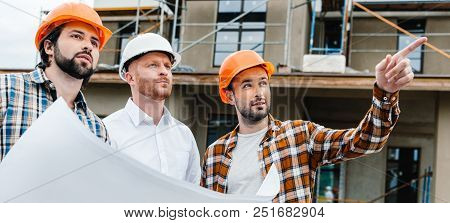 Wide Shot Of Group Of Architects With Building Plan Standing In Front Of Construction Site And Looki