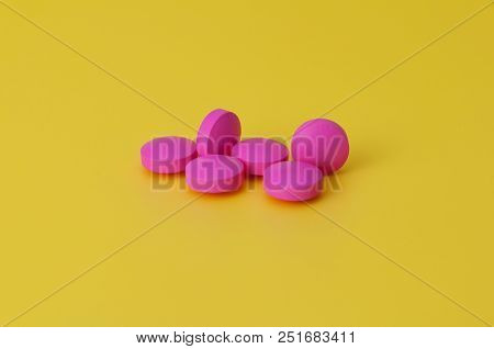 Several Large Bright Pink Tablets On A Yellow Background. In The Center Of The Image.