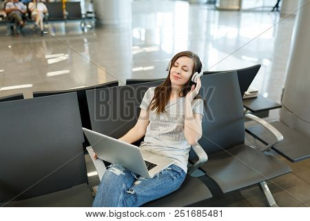 Young Relaxed Traveler Tourist Woman With Headphones Listening Music Working On Laptop, Wait In Lobb
