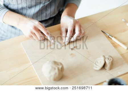 Master of pottery cutting thin piece of clay into small pieces on wooden board