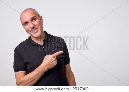Mature Hispanic Man Pointing Aside Copy Space. Handsome Elder Man In Black Shirt Looking At Camera A