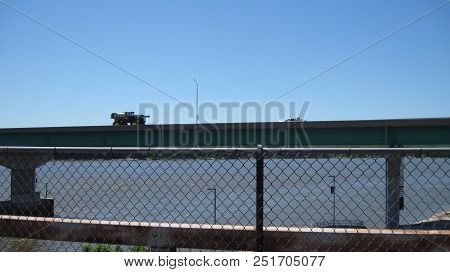 A Bridge With 2 Trucks Driving Over The Mississippi River As Seen From A Fenced Walking Bridge  In K