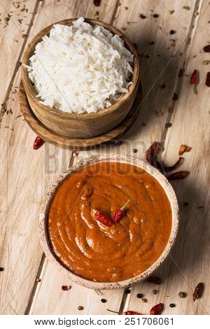 high angle view of a bowl with a chicken korma curry and a bowl with cooked rice on an off-white wooden table