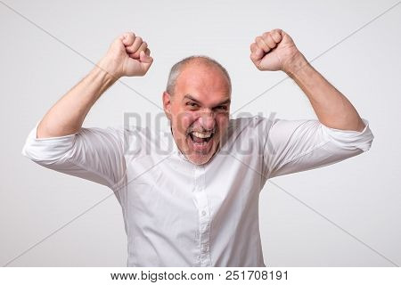Mature Hispanic Man Is Happy With His Win. He Is Holding His Fists And Shout Wow. Sign Of Victory Is