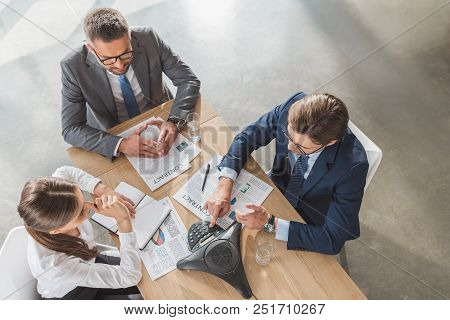 High Angle View Of Business People Using Speakerphone During Conversation At Modern Office