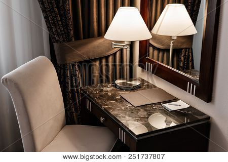 Interior Hotel Apartment, Comfortable Room, Mirror And Desk. Folder For Notes And Lamp Standing On A