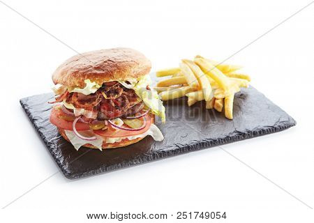 Fresh Beef Burger with Bacon, Fried Onions, Tomato Sauce, Pickled Cucumbers, Green Lettuce, Cheese and French Fries Garnish. Hamburger or Beefburger on Natural Black Stone Plate Isolated on White