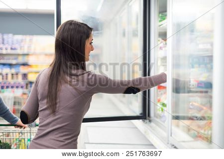 Woman taking deep frozen food from a freezer in a supermarket