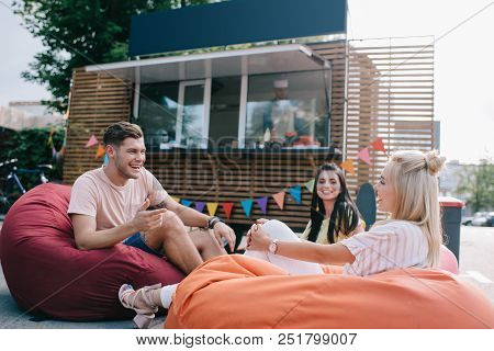 Happy Young Friends Talking While Sitting On Bean Bag Chairs Near Food Truck