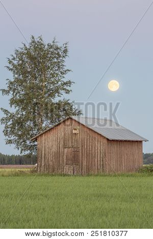Barn In Farmfield By Tree With A Full Moon.