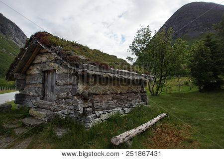 A Small House Made Of Trunks Of Large Trees, The Earthen Roof Overgrew With Grass, Near The Mountain
