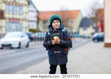 Little Kid Boy With Eye Glasses On The Way To The School And Eating Fresh Apple. Child On A Street. 