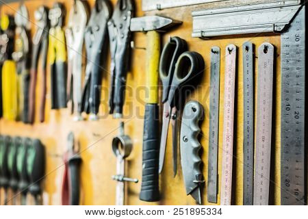 Tools And Devices Hanging On Workshop Wall. Rulers, Cutting Knives, Scissors And Other Objects Well 