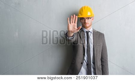 Young redhead man wearing architect outfit and helment with open hand doing stop sign with serious and confident expression, defense gesture