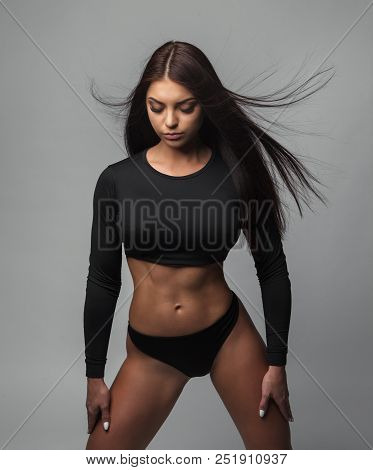 Attractive Sporty Woman In Black Bikini Posing On Grey Background. Photo Of Brunette Woman With Slim