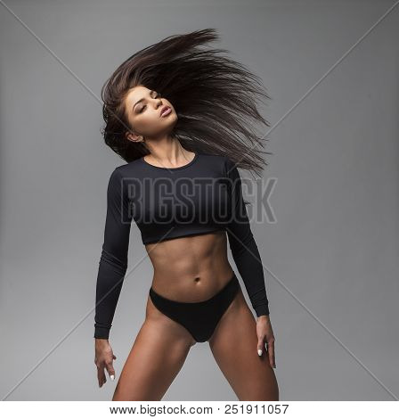 Attractive Sporty Woman In Black Bikini Posing On Grey Background. Photo Of Brunette Woman With Slim