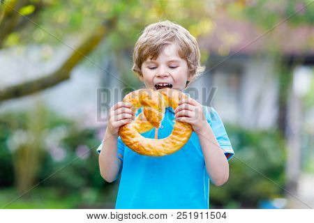 Adorable Little Kid Boy Eating Huge Big Bavarian German Pretzel. Happy Blond Child Enjoying Tasteful