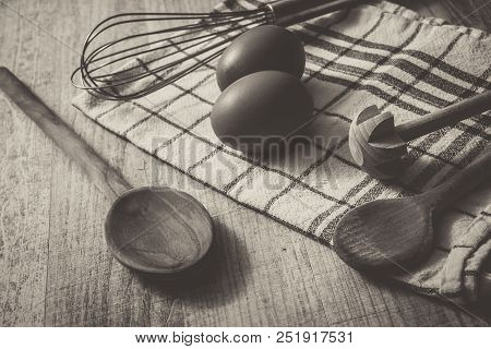 A Monochrome Kitchen Setting With 2 Eggs, Towel, Wooden Spoon And Querl And An Eggbeater On A Table