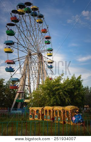 An Old Colored Ferris Wheel And A Train Ride For Children In The City Park