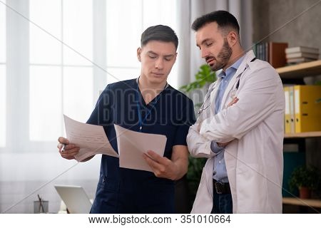 Two Young Male Doctors Discussing Medical Case In The Staffroom During Changeover