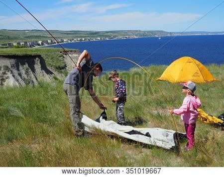 Camping, Hiking. Dad Teaches Children To Set Up A Tent On A Rocky Beach In The Spring On A Sunny Day