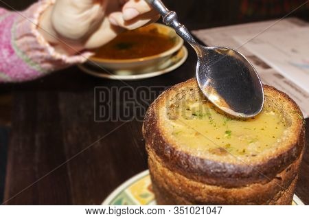 A Woman Eats Homemade Soup From A Plate Of Bread.
