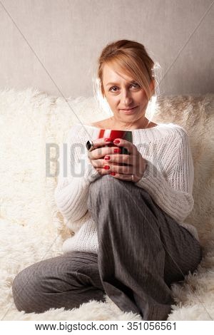 Portrait Of An Adult Woman In A Cozy Room On The Couch With A Cup Of Tea / Coffee.