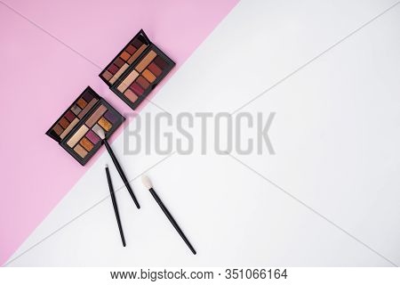 Top View Of Two Colorful Eyeshadow Palletes And Natural Makeup Brushes On White And Pink Background.