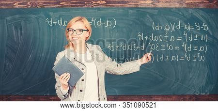 Teacher Smart Woman With Book Explain Topic Near Chalkboard. School Teacher Explain Things Well And 