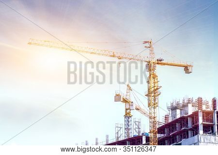 Building Under Construction With Hoisting Cranes Working To Move Building Materials Under The Blue S