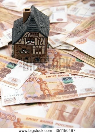 A Ceramic House Stands On A Pile Of Five Thousand Ruble Bills. Symbol Of Success, Improvement Of Liv