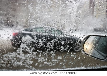 Drops On The Glass. View From The Car Window During Rain And Wet Snow. Blurred Background Of Cars On