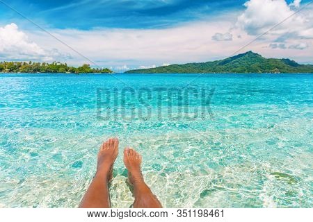 Relax feet selfie woman lying in turquoise crystalline blue water on French Polynesia motu beach vacation summer. Woman relaxing on tropical travel destination swimming sun tanning.