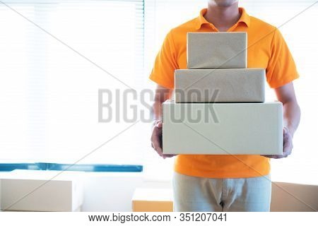 Young Delivery Asian Man In Uniform Holding And Carrying Stack Of Cardboard Postel In Office.