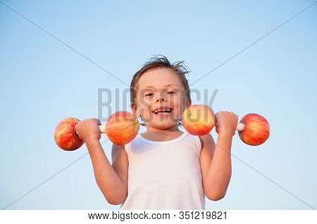 Strong Healthy Active Little Kid In White Tank Top Lifting Heavy Dumbbells From Apples On Blue Sky B
